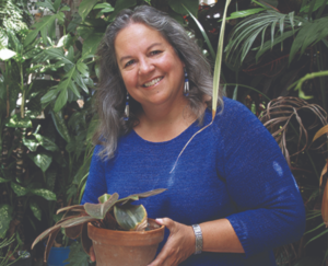 Photo of Robin Wall-Kimmerer in a blue sweater holding a potted plant